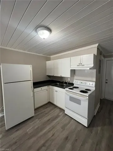Kitchen with white appliances, ornamental molding, white cabinetry, dark wood finished floors, and dark countertops