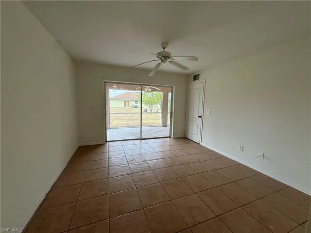 Empty room with ceiling fan, dark tile patterned floors, and baseboards