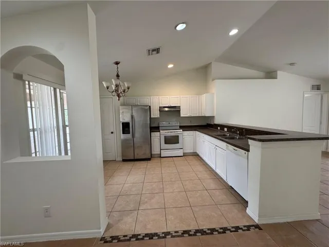 Kitchen featuring white appliances, a sink, under cabinet range hood, light tile patterned floors, and arched walkways