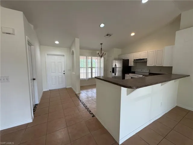 Kitchen with white range with electric cooktop, stainless steel refrigerator with ice dispenser, a chandelier, under cabinet range hood, and dark countertops