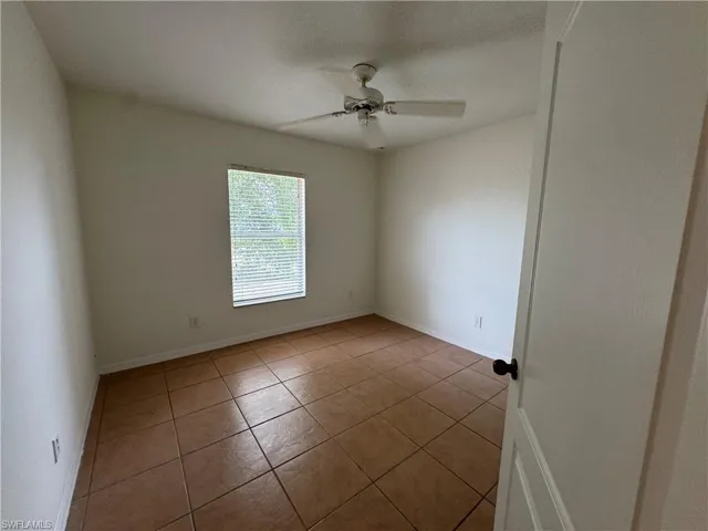 Tiled empty room featuring a ceiling fan and baseboards