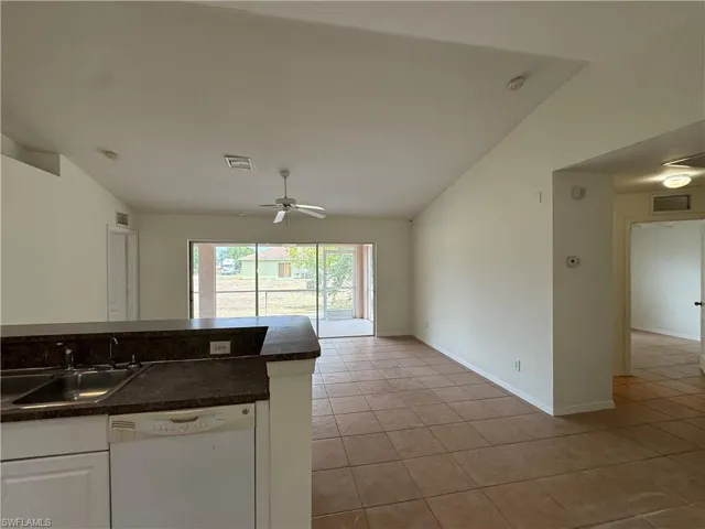 Kitchen with dishwasher, a sink, dark countertops, vaulted ceiling, and light tile patterned floors