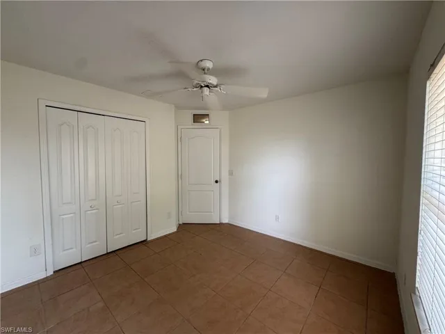 Unfurnished bedroom with tile patterned floors, a closet, baseboards, and a ceiling fan