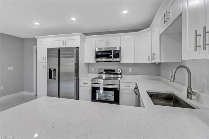 Kitchen featuring white cabinetry, appliances with stainless steel finishes, light stone countertops, and sink