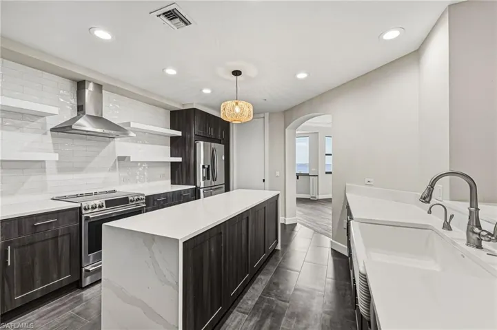 This kitchen has been thoughtfully reimagined, showcasing an oversized island with striking waterfall quartz countertops, a farmhouse sink, and stainless steel appliances. A spacious walk-in pantry and distinctive storage shelving provide exceptional functionality, while a classic subway tile backsplash, warm wood cabinetry, and custom lighting complete the space with refined style.
