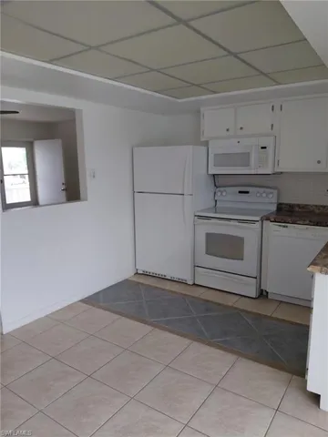 Kitchen featuring white appliances, white cabinets, light tile patterned floors, and backsplash