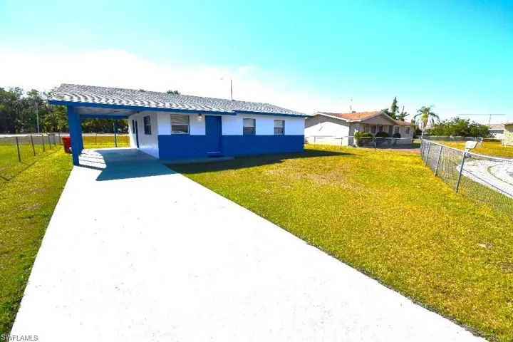 Single-story residence featuring a blue and white exterior, an attached carport, a paved driveway, and a chain-link fence