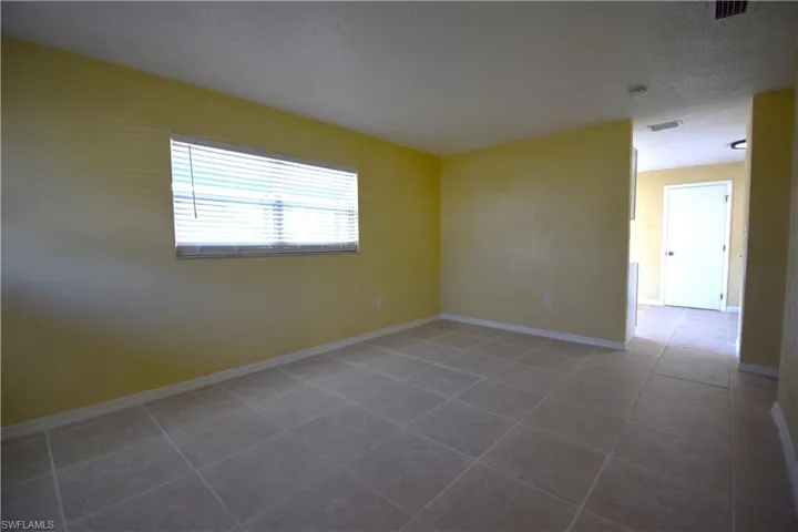 Spacious room featuring neutral tile flooring, a window with horizontal blinds, light yellow walls, and white baseboards