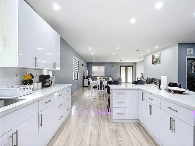 Kitchen with open floor plan, white cabinetry, a kitchen bar, light stone counters, and recessed lighting