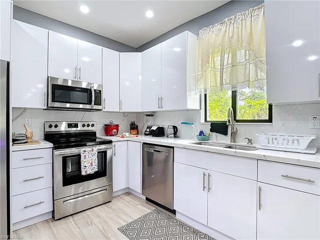 Kitchen with appliances with stainless steel finishes, white cabinetry, backsplash, light wood-style floors, and recessed lighting