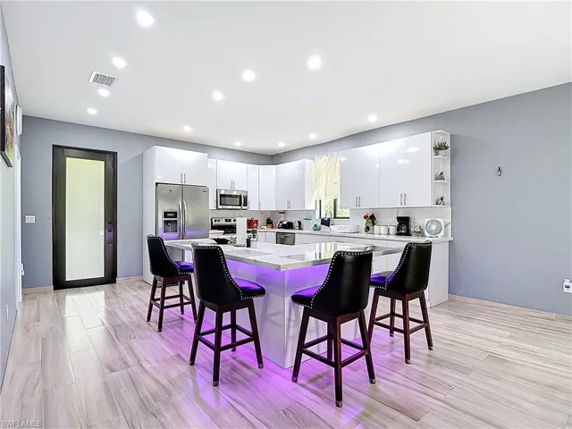 Kitchen featuring a kitchen island, white cabinets, a breakfast bar, light wood-style floors, and recessed lighting