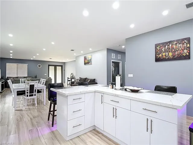 Kitchen featuring a breakfast bar area, open floor plan, recessed lighting, white cabinetry, and light stone countertops