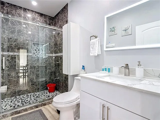 Bathroom featuring vanity, a marble finish shower, and light wood-style flooring