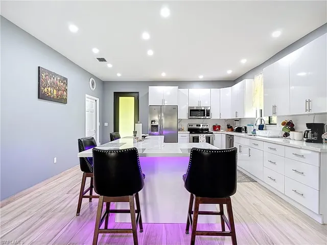 Kitchen with a breakfast bar, stainless steel appliances, a kitchen island, white cabinetry, and recessed lighting
