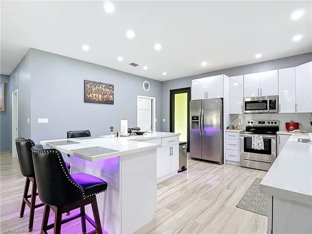 Kitchen with appliances with stainless steel finishes, a breakfast bar, white cabinets, recessed lighting, and light stone countertops