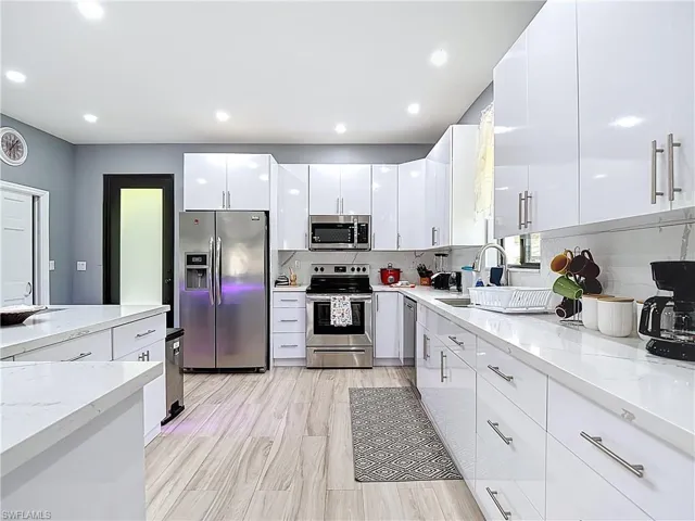 Kitchen with appliances with stainless steel finishes, white cabinets, light stone counters, recessed lighting, and modern cabinets