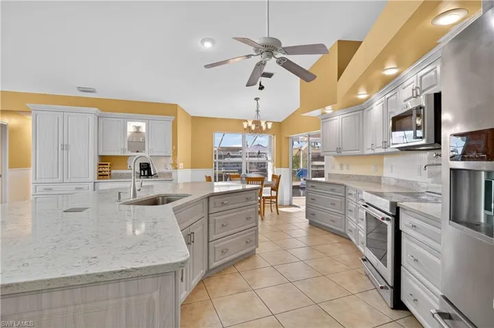 Kitchen with stainless steel appliances, light stone counters, glass insert cabinets, a chandelier, and hanging light fixtures