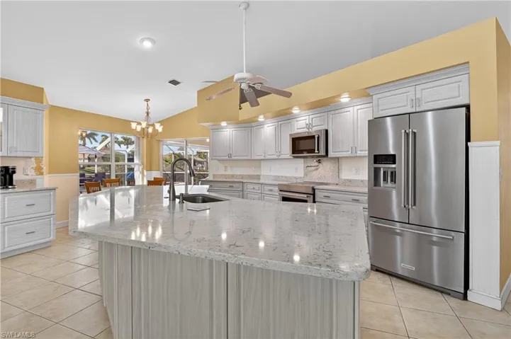 Kitchen with stainless steel appliances, an island with sink, light tile patterned floors, light stone counters, and a chandelier