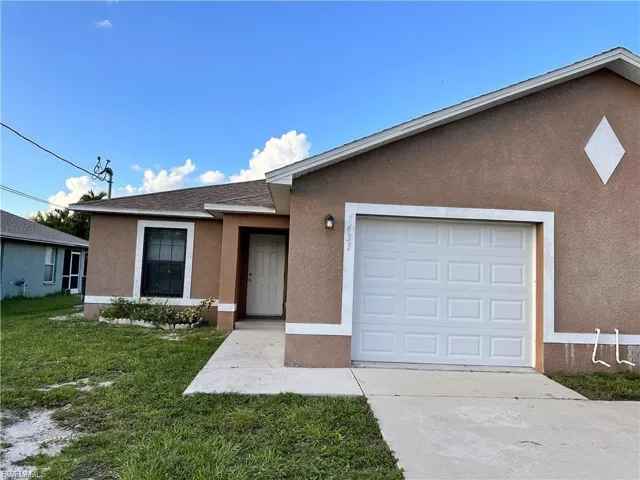 Ranch-style home with stucco siding, an attached garage, driveway, and a front lawn