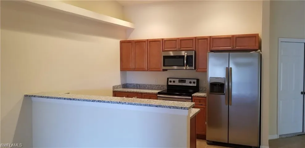 Kitchen featuring stainless steel appliances, light stone counters, wood finish cabinets, and a peninsula
