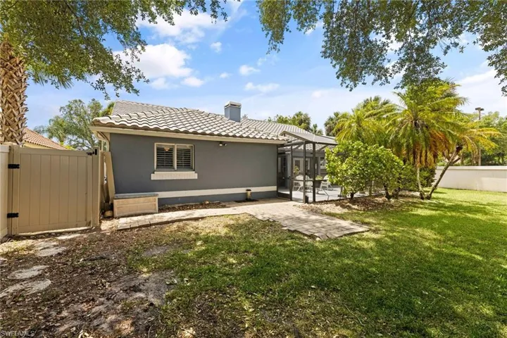 Rear view of house with a gate, fence, glass enclosure, a yard, and a tiled roof
