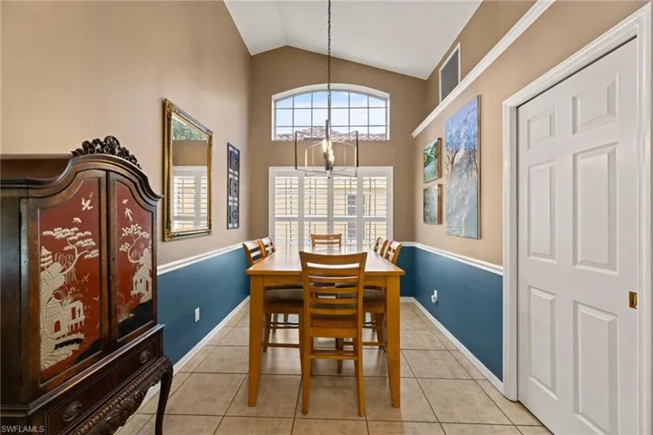 Dining space featuring light tile patterned floors, high vaulted ceiling, baseboards, and an inviting chandelier