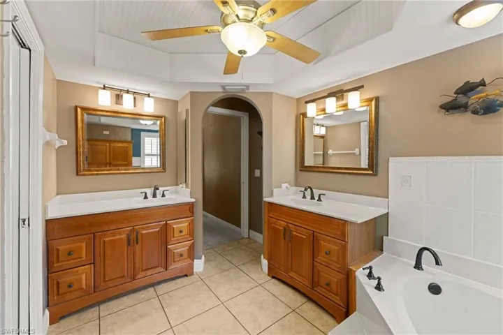 Full bathroom featuring tile patterned flooring, a raised ceiling, two vanities, and a sink