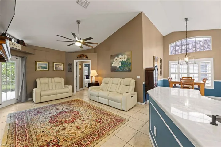 Living room featuring visible vents, baseboards, light tile patterned flooring, high vaulted ceiling, and a ceiling fan