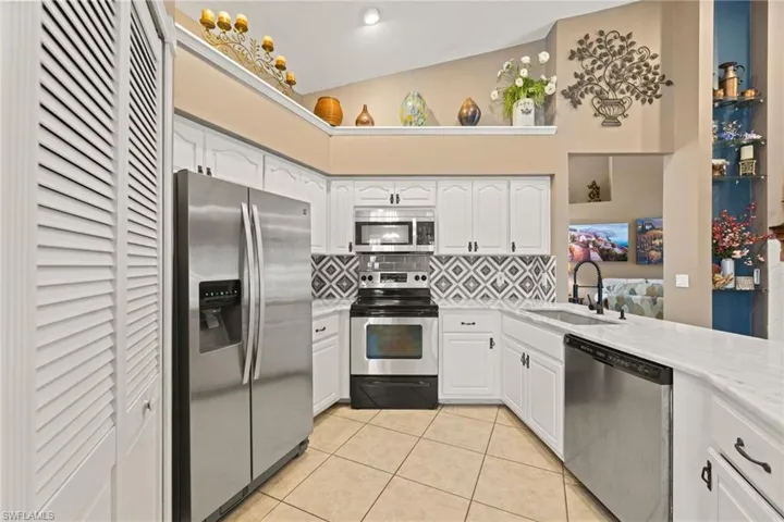 Kitchen with tasteful backsplash, light countertops, light tile patterned floors, appliances with stainless steel finishes, and a sink