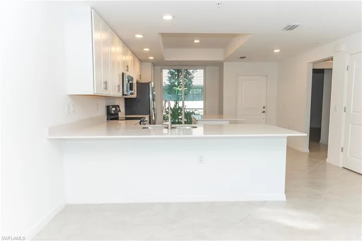 Kitchen with kitchen peninsula, black range oven, a tray ceiling, sink, and light tile patterned flooring