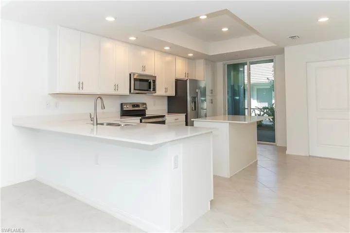 Kitchen featuring kitchen peninsula, stainless steel appliances, sink, white cabinets, and a center island