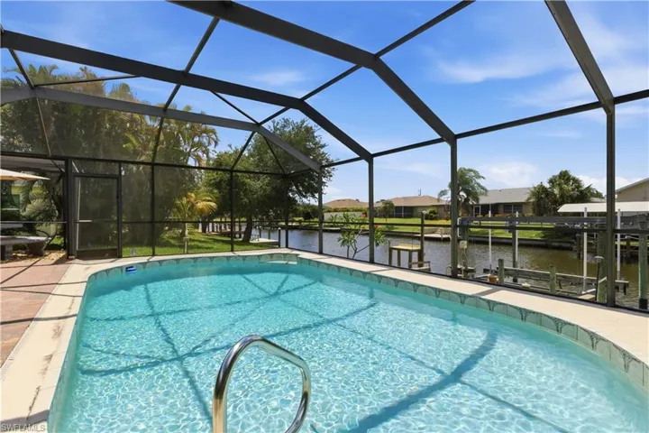 Screened swimming pool with a curved edge and integrated grab rail, featuring a surrounding paver patio