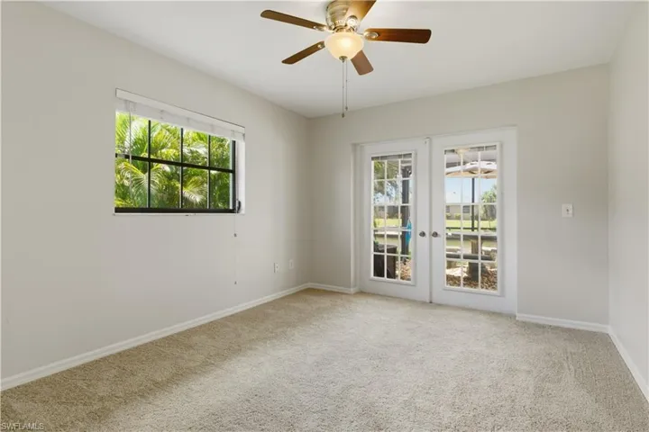 White walls with neutral carpeting, French doors, and a window with palm tree foliage