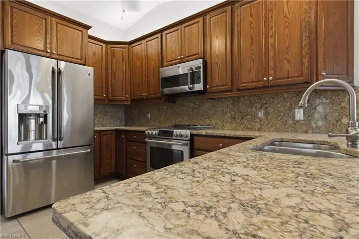 Kitchen featuring extensive wood cabinetry, stone countertops with integrated sink, stainless steel appliances, and a matching stone backsplash