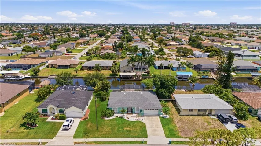 Aerial perspective showcasing multiple properties, including a prominent residence with a dark shingle roof and an attached garage