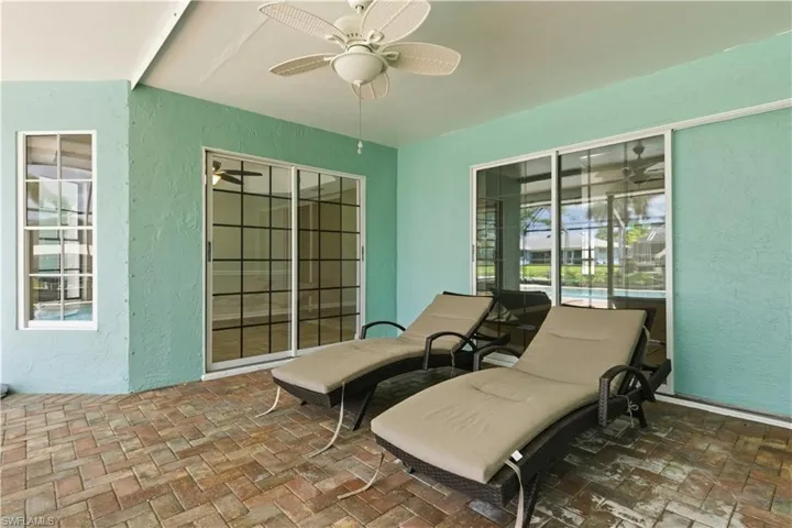 Covered patio featuring an outdoor ceiling fan, multi-tone paver flooring, and sliding glass doors with grid detailing