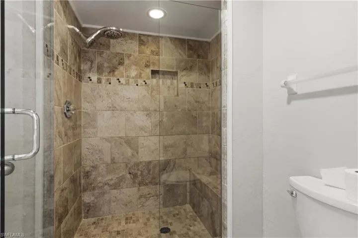 Glass-enclosed shower featuring natural stone-look tile, a built-in bench, a recessed shower niche, and a rain showerhead