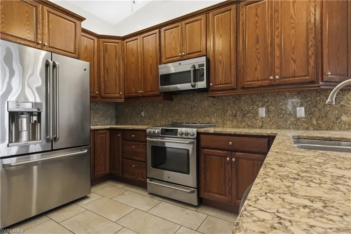 Kitchen featuring wood cabinetry, stainless steel appliances, speckled stone countertops, and tile flooring
