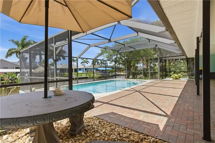 Screened pool enclosure featuring a rectangular swimming pool with integrated steps, a paver patio, and rock landscaping