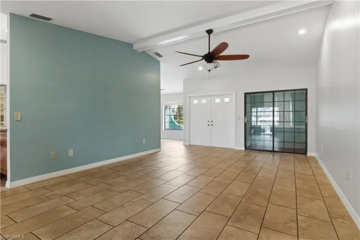 Spacious interior featuring neutral tile flooring, vaulted ceilings with exposed beams, and a modern ceiling fan