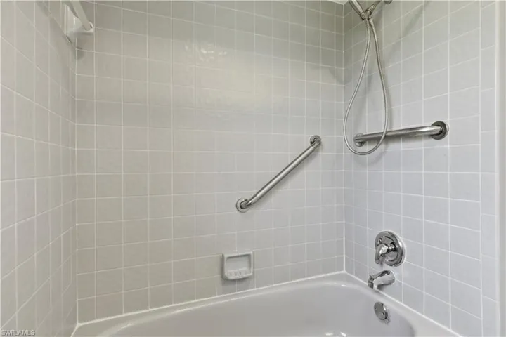 Bathtub with light gray square wall tiles, chrome fixtures, and two installed grab bars