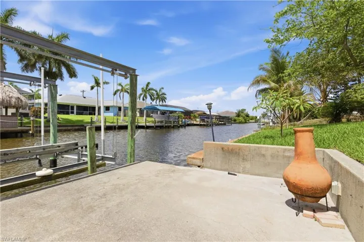 Concrete dock featuring a boat lift, canal access, and tropical landscaping