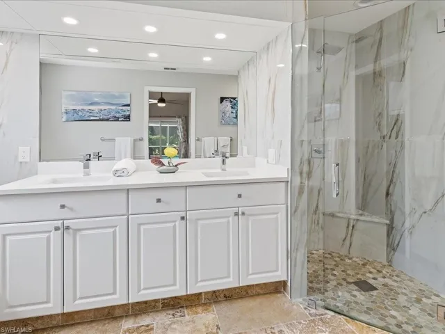 Full bath with double vanity, a marble finish shower, recessed lighting, and ceiling fan