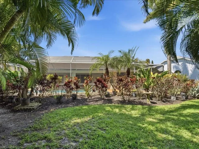View of green lawn with a sunroom, an outdoor pool, and a lanai