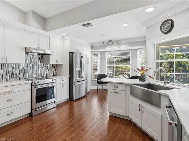 Kitchen with stainless steel appliances, light stone counters, white cabinets, ornamental molding, and dark wood-type flooring