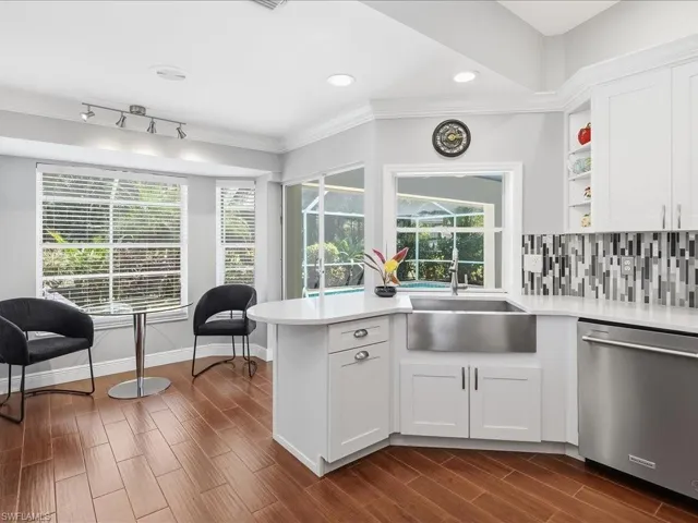 Kitchen featuring dishwasher, backsplash, wood tiled floors, white cabinetry, and ornamental molding