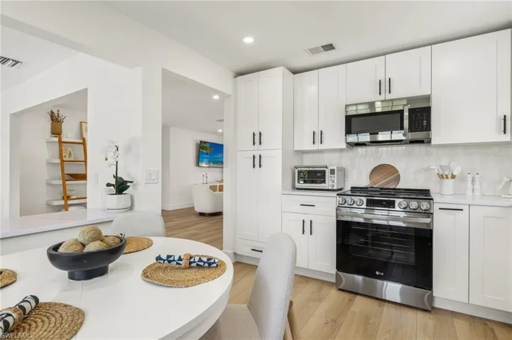 Kitchen with white cabinetry, light wood-type flooring, stainless steel appliances, and tasteful backsplash