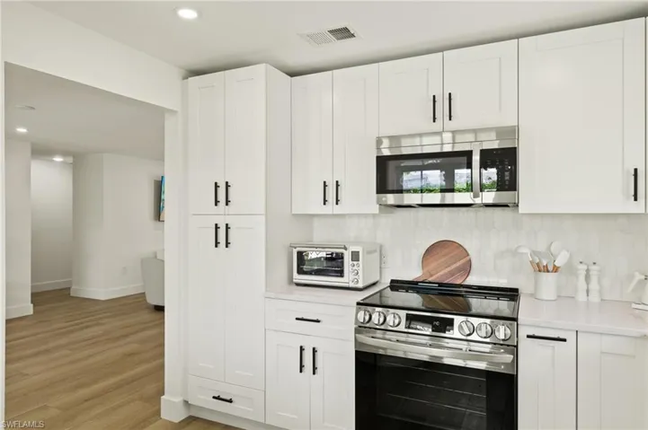 Kitchen featuring white cabinets, appliances with stainless steel finishes, light hardwood / wood-style floors, and tasteful backsplash