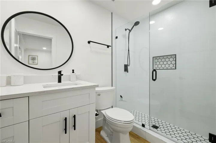 Bathroom with hardwood / wood-style floors, a shower with shower door, vanity, and toilet