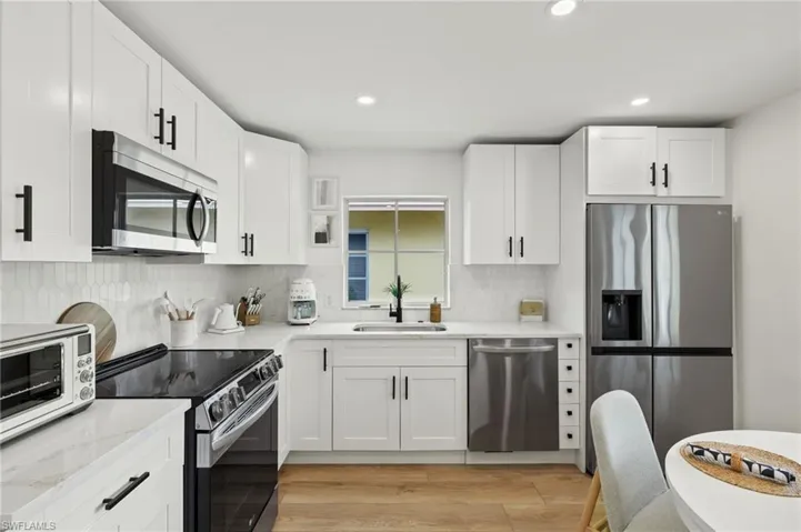 Kitchen with white cabinetry, appliances with stainless steel finishes, sink, and light hardwood / wood-style flooring